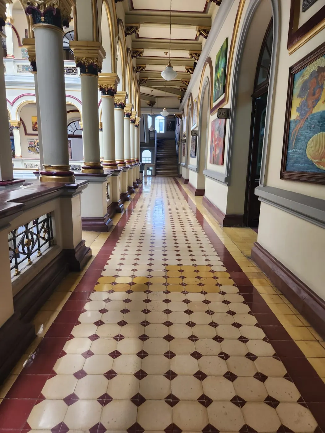 A tiled, arched corridor lined with paintings in a historic downtown building