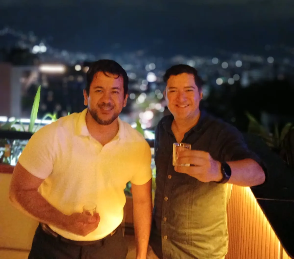 Deux voyageurs trinquent dans un bar sur un toit, avec les lumières de Medellín derrière eux